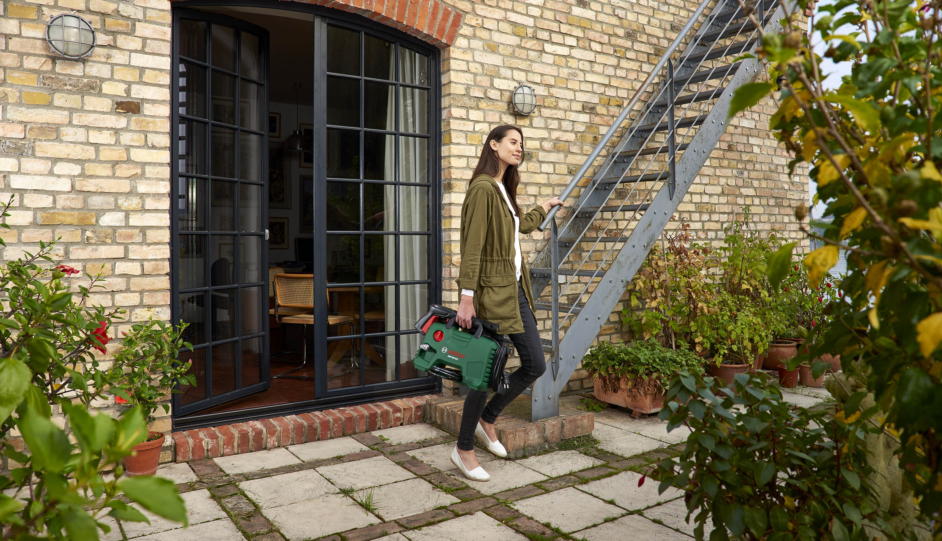 Young woman carrying a Bosch pressure washer up outside stairs in Berlin