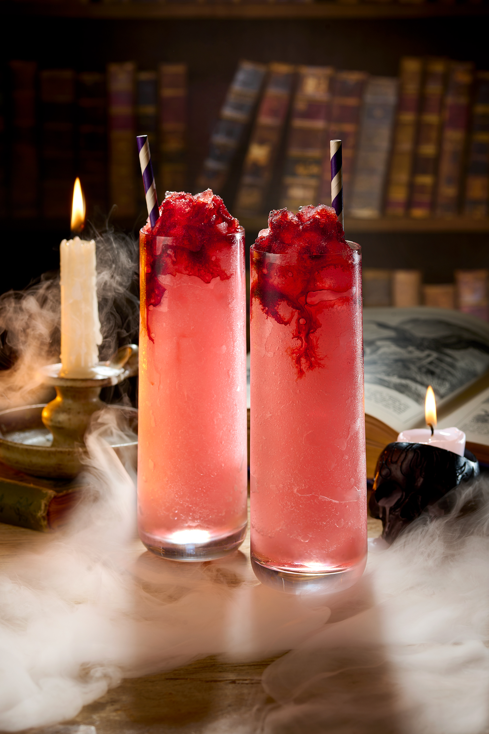 two cocktails in a smokey enviroment with candles and bookcases in the background